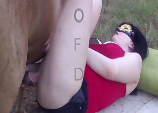 Red outfit lady wears a mask while fucking a brown stallion outdoors